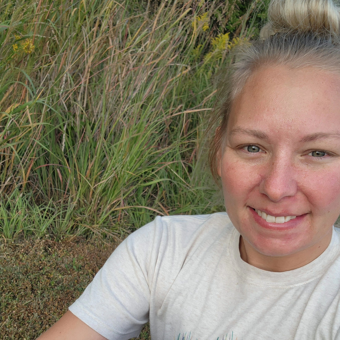 Woman is sitting at the edge of a trail next to little bluestem grass.